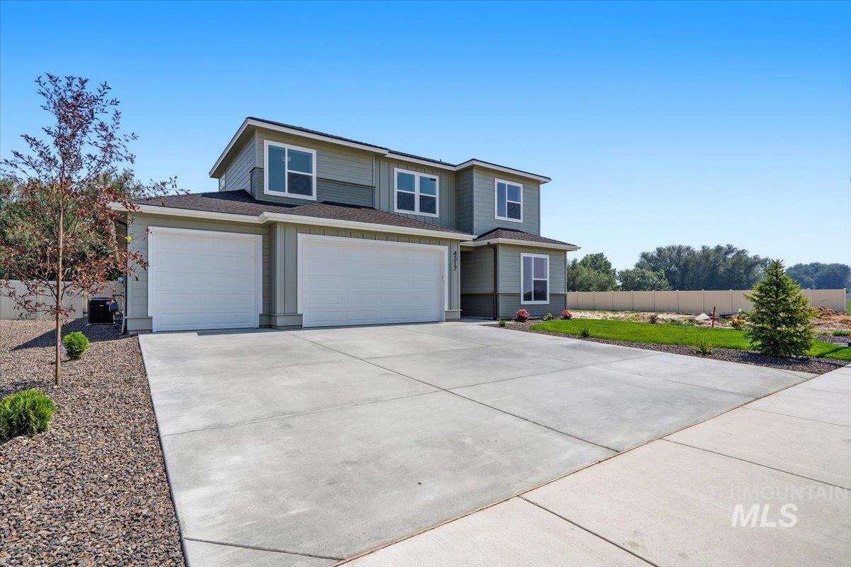 4317 Tropic Way Caldwell, ID 83607 - Photo 1 of 43 Modern exterior with a light gray and dark gray siding, a two-car garage, an additional single-car garage, a concrete driveway, and a landscaped front yard with a young evergreen tree