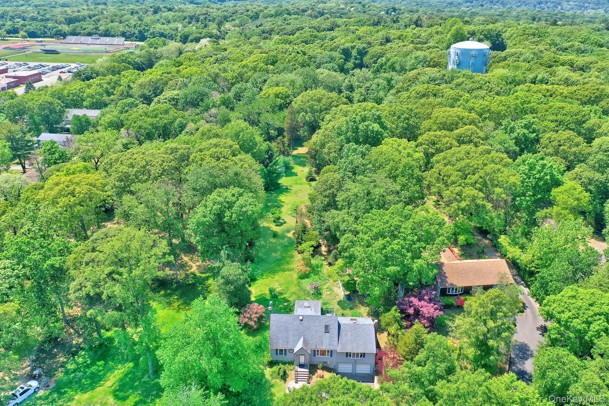 100 Elwood Road Northport, NY 11768 - Photo 31 of 39 Expansive property featuring a grey-sided residence with a dark roof and a separate, darker-roofed structure, surrounded by abundant mature trees and verdant landscaping,