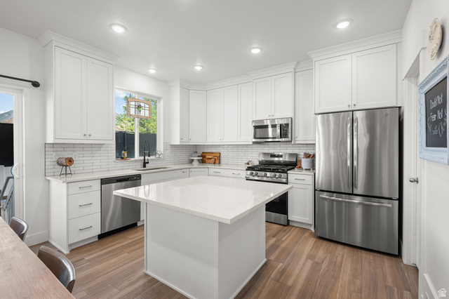 2706 West Maple Street, Unit 285 Mapleton, UT 84664 - Photo 11 of 36 Modern kitchen featuring white shaker cabinetry, stainless steel appliances, a center island with a light-toned countertop, subway tile backsplash, and wood-finish flooring