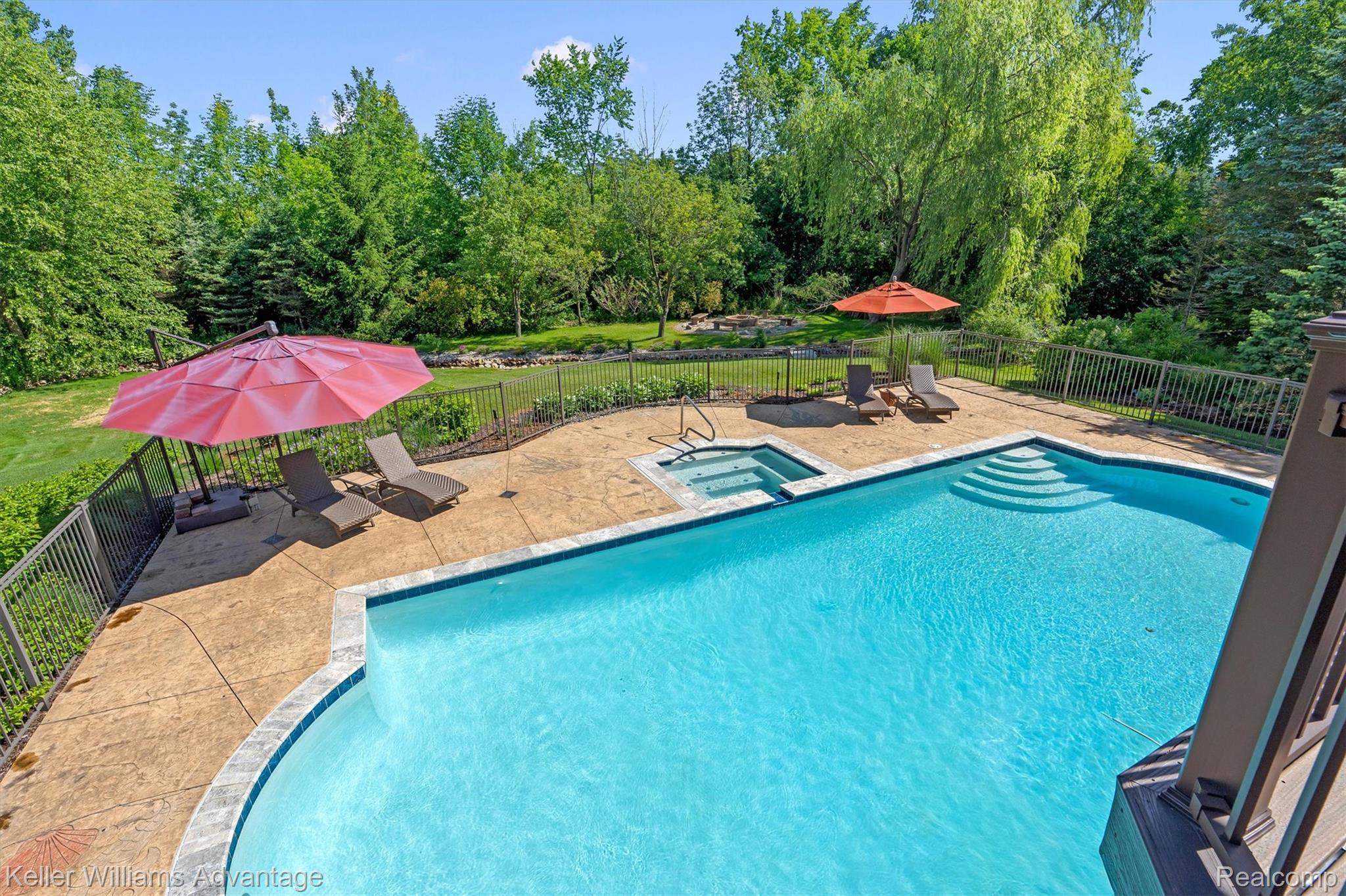 22878 Tree Top Court South Lyon, MI 48178 - Photo 43 of 75 Outdoor swimming pool with integrated spa, surrounded by stamped concrete decking and a dark metal fence