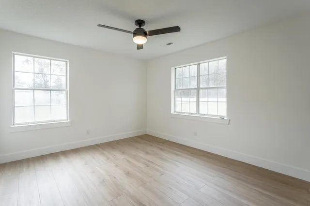 an empty room with wooden floor fan and windows