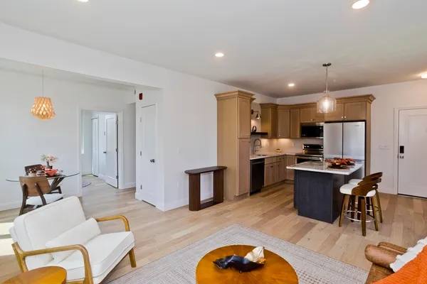 a living room with stainless steel appliances furniture wooden floor and kitchen view