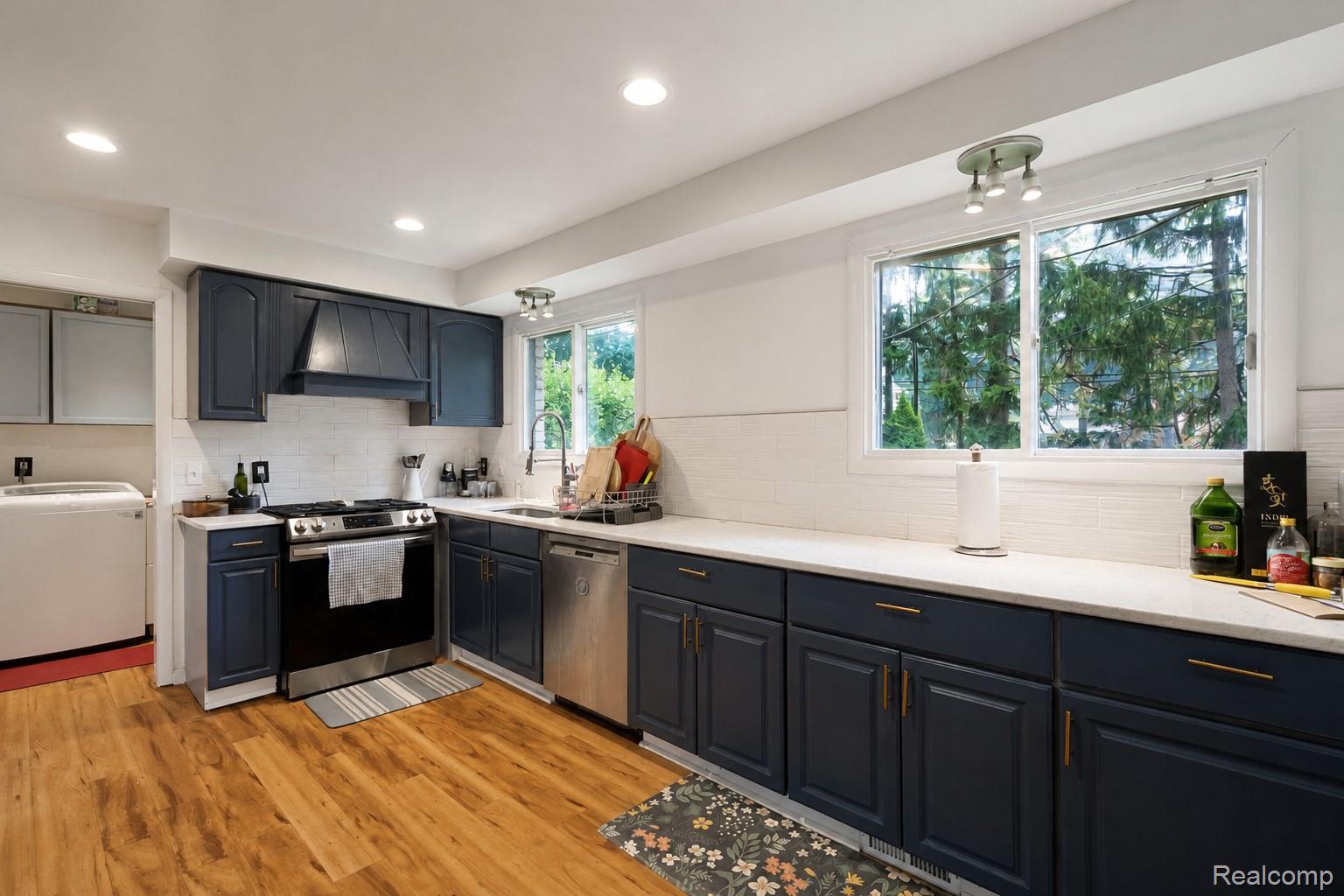 2247 West Maple Road Birmingham, MI 48009 - Photo 24 of 46 Modern kitchen featuring dark blue cabinetry, light-colored countertops, stainless steel appliances, a white subway tile backsplash, and wood-finish flooring