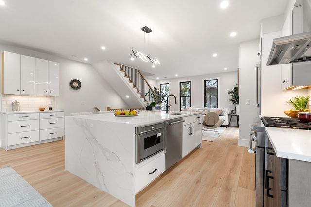 a large white kitchen with a stove a sink a refrigerator and white cabinets with wooden floor