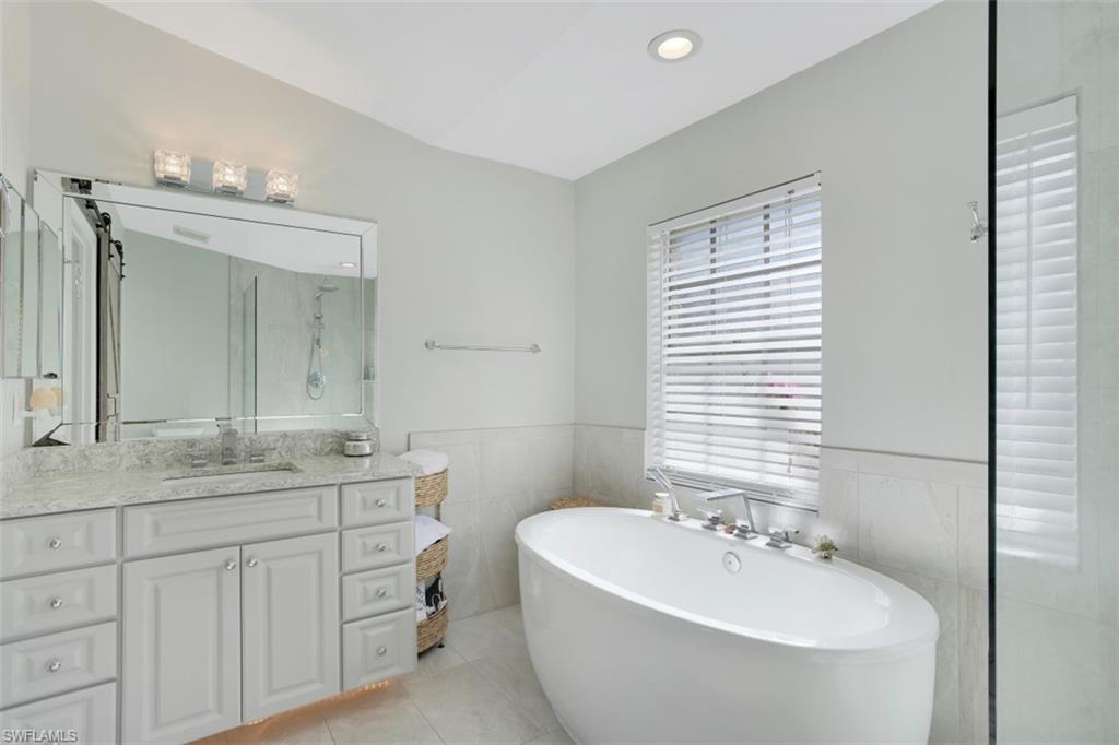 7311 Mill Pond Circle Naples, FL 34109 - Photo 15 of 22 a bathroom with a double vanity sink large mirror and a bathtub