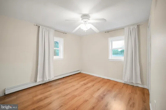 an empty room with wooden floor fan and windows