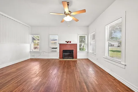 a view of an empty room with wooden floor fireplace and a window