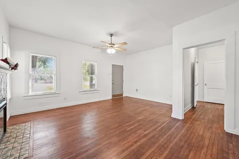 an empty room with wooden floor chandelier fan and windows
