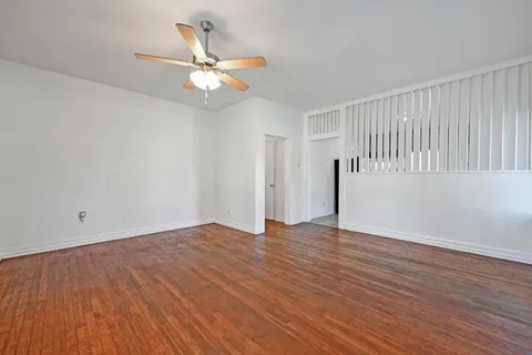 a view of an empty room with wooden floor and a ceiling fan