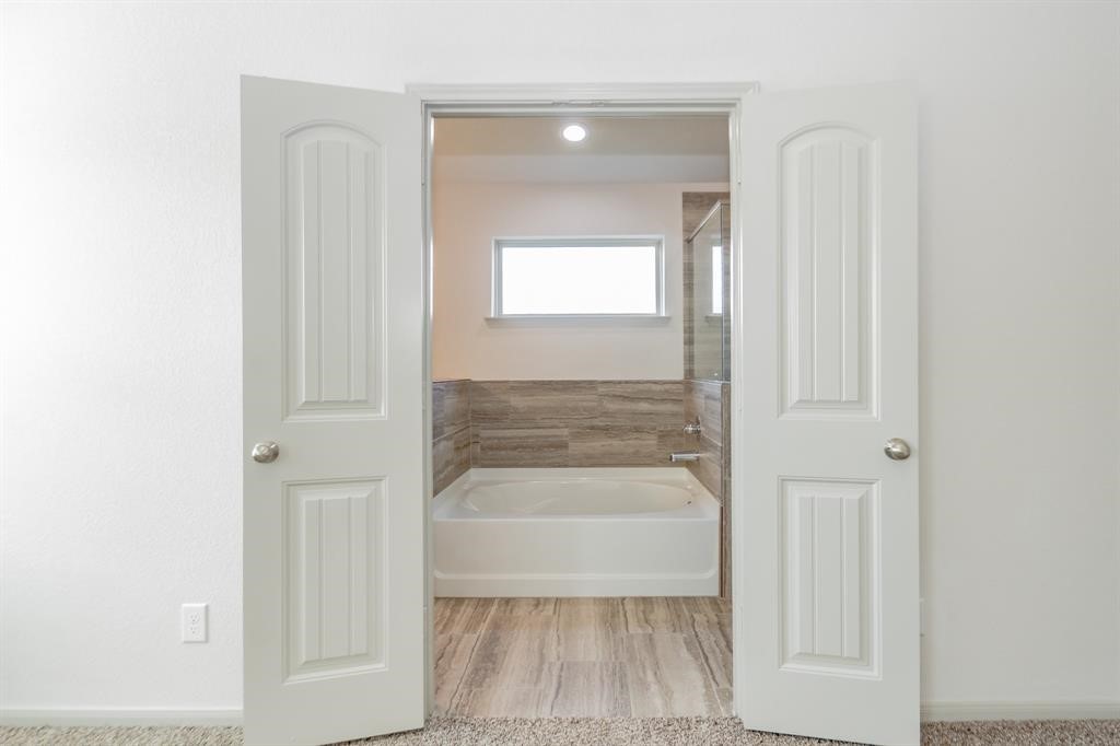 6447 Escondido Drive Rosharon, TX 77583 - Photo 9 of 16 Step into luxury through these double doors that lead to the elegant primary bathroom. This space combines style and functionality with a soaking tub, tiled shower, and ample natural light. The seamless connection to the bedroom ensures your private oasis is always within reach.