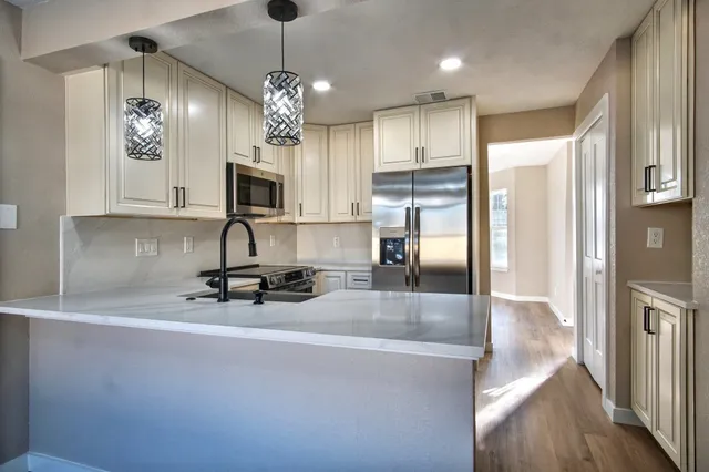 a view of a kitchen with kitchen island a sink wooden floor and stainless steel appliances