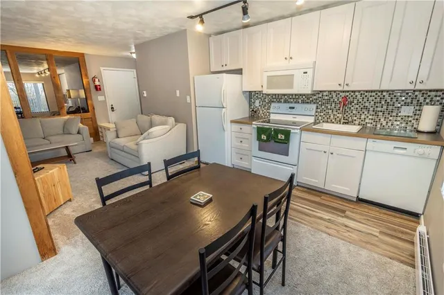 a kitchen with stainless steel appliances granite countertop a stove a refrigerator a sink a dining table and chairs with wooden floor