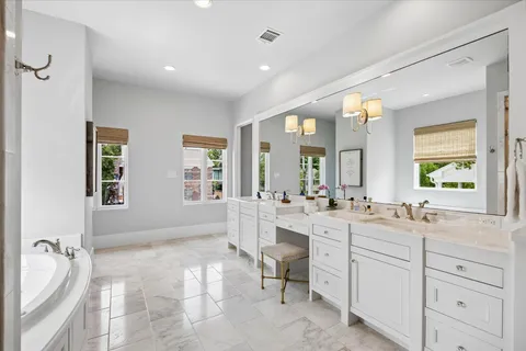 a spacious bathroom with a double vanity sink a mirror a bathtub and next to a window