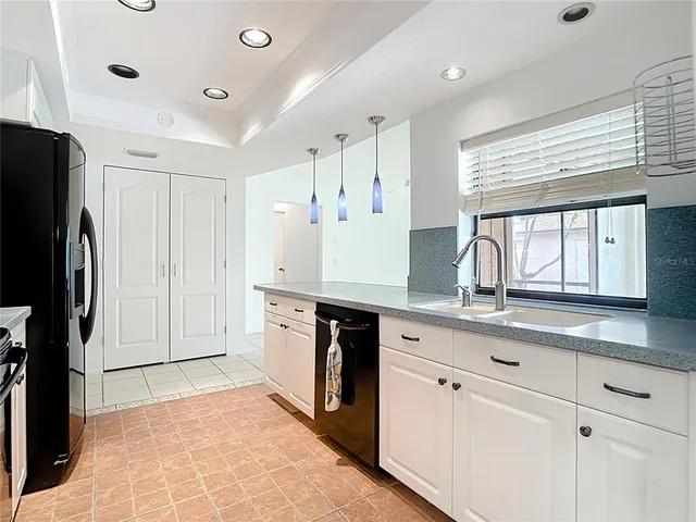 a kitchen with granite countertop a refrigerator a sink and white cabinets