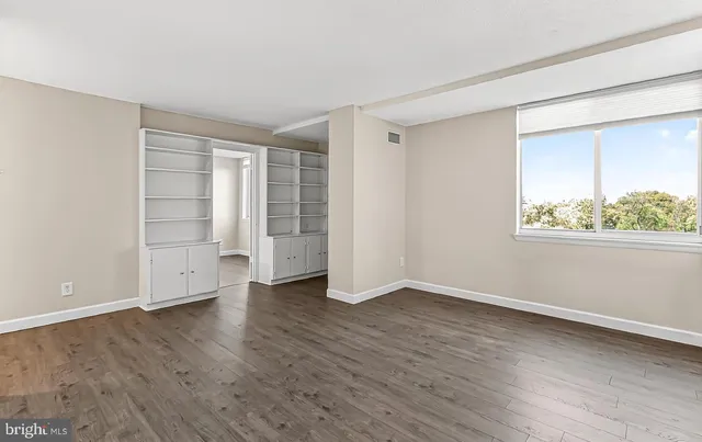 an empty room with wooden floor cabinet and windows