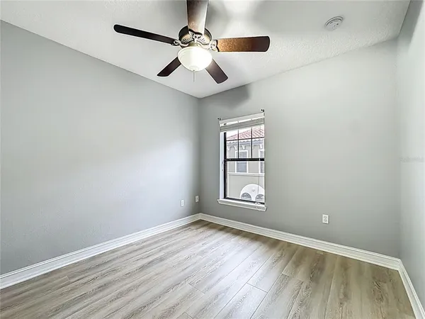 an empty room with wooden floor chandelier fan and windows