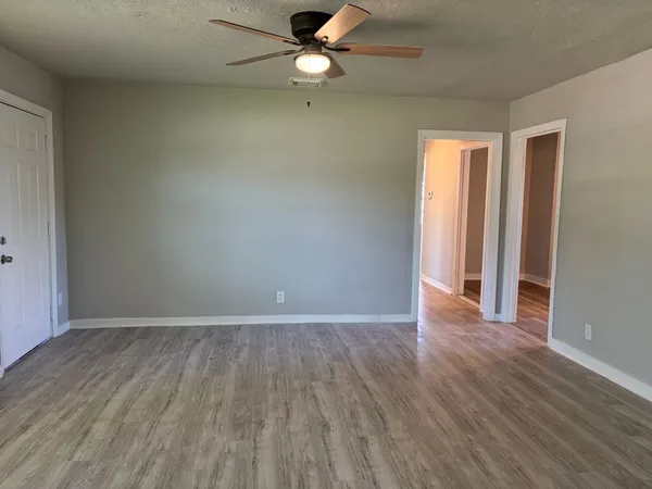 an empty room with wooden floor fan and windows