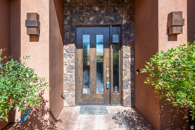 322 340 E Street Ivins, UT 84738 - Photo 4 of 61 Entryway featuring a wood-panel door with vertical glass inserts, stone veneer detailing, stucco exterior, and modern wall sconces