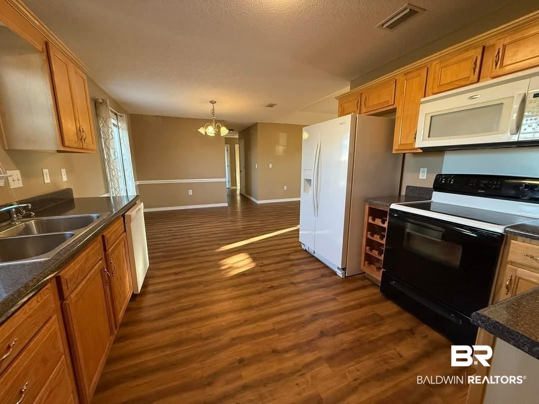 8912 Sherman Road Foley, AL 36535 - Photo 26 of 35 Kitchen featuring white appliances, visible vents, dark countertops, dark wood-style flooring, and a sink