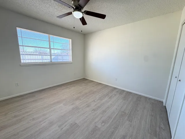 an empty room with wooden floor ceiling fan and windows