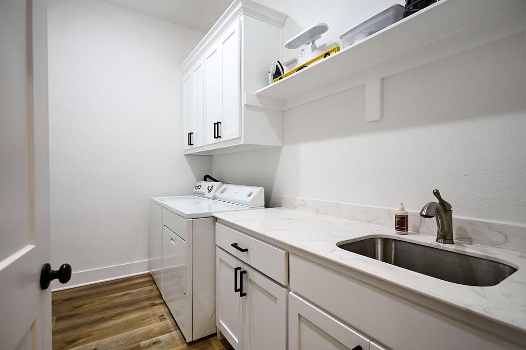 358 Glade Valley Road Azle, TX 76020 - Photo 26 of 35 Utility room featuring wood-finish flooring, white cabinetry with black hardware, a stainless steel sink with a gooseneck faucet, a light-toned countertop, and open shelving