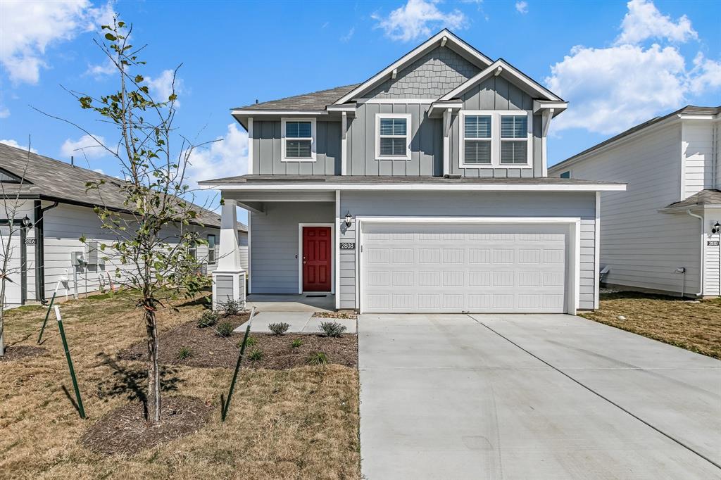 2808 Totley Road Manor, TX 78653 - Photo 1 of 21 Two-story residence featuring light gray siding, a two-car garage, a covered front porch with white columns, and a red front door