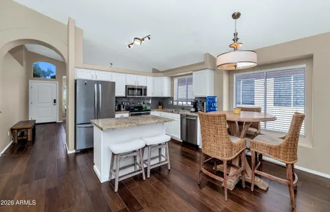 a kitchen with stainless steel appliances granite countertop a refrigerator a stove a sink a dining table and chairs with wooden floor