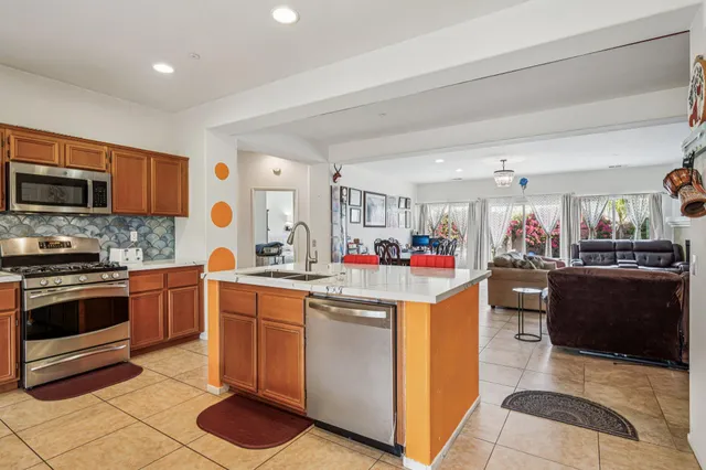 a living room with stainless steel appliances furniture a rug and a kitchen view