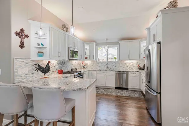 a kitchen with stainless steel appliances granite countertop a refrigerator a sink dishwasher a stove with white cabinets and wooden floor