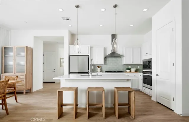 a large kitchen with stainless steel appliances kitchen island granite countertop a table chairs and a refrigerator
