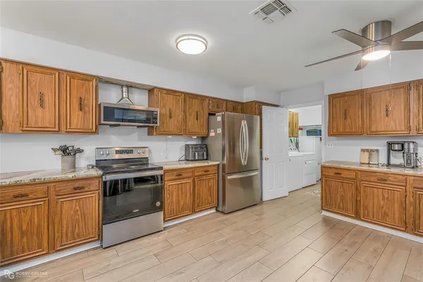 a kitchen with stainless steel appliances granite countertop a stove top oven a refrigerator a sink and dishwasher with wooden cabinet