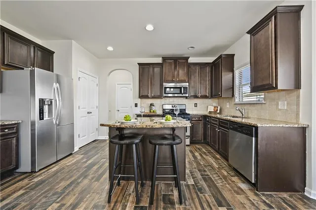 a kitchen with kitchen island granite countertop wooden floors wooden cabinets a refrigerator and a stove