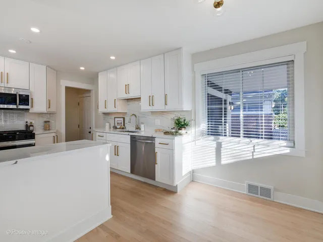 a kitchen with stainless steel appliances granite countertop a stove a sink a refrigerator white cabinets and a wooden floor