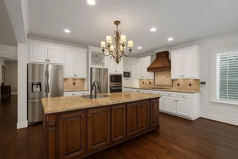 a kitchen with stainless steel appliances granite countertop a refrigerator a sink dishwasher a oven with white cabinets and wooden floor