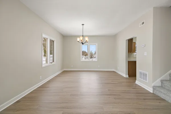 an empty room with wooden floor chandelier and windows