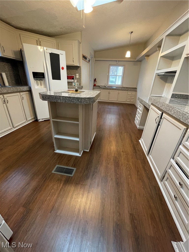 Kitchen with dark wood-type flooring, refrigerator, vaulted ceiling, decorative backsplash, and decorative light fixtures
