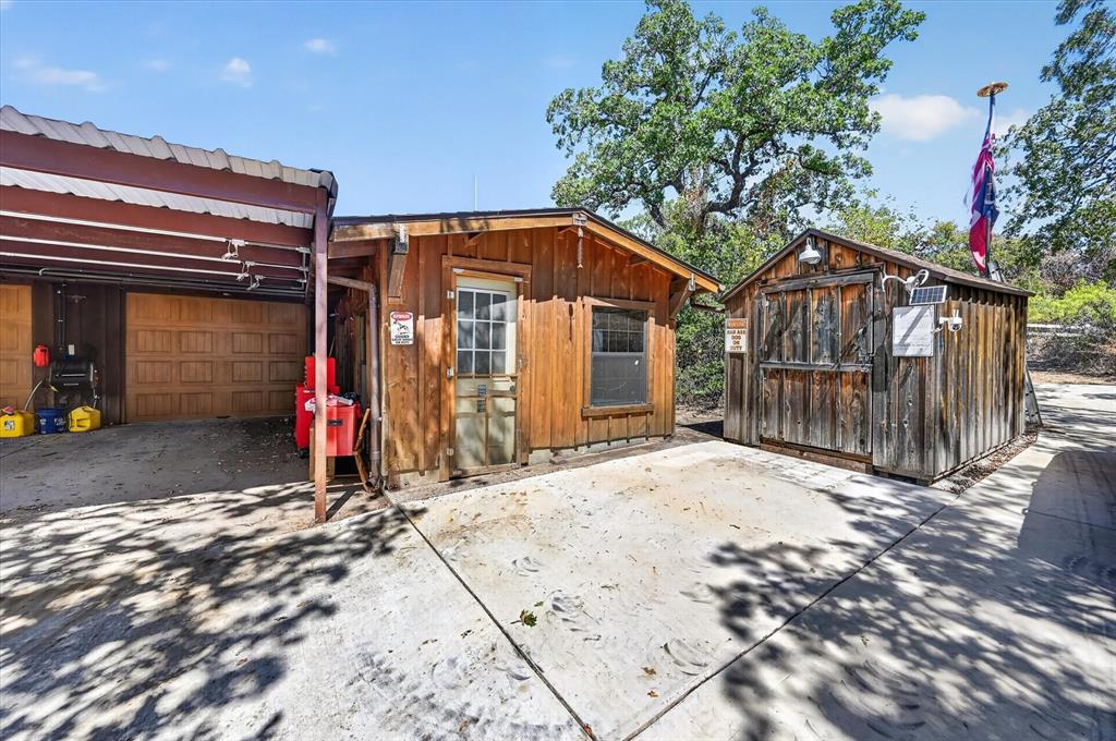 1623 3 Skillet Road Springtown, TX 76082 - Photo 31 of 40 Wood-sided detached structures with a covered parking area featuring a roll-up garage door, a separate building with a paneled door and window, and an additional shed with a solar panel
