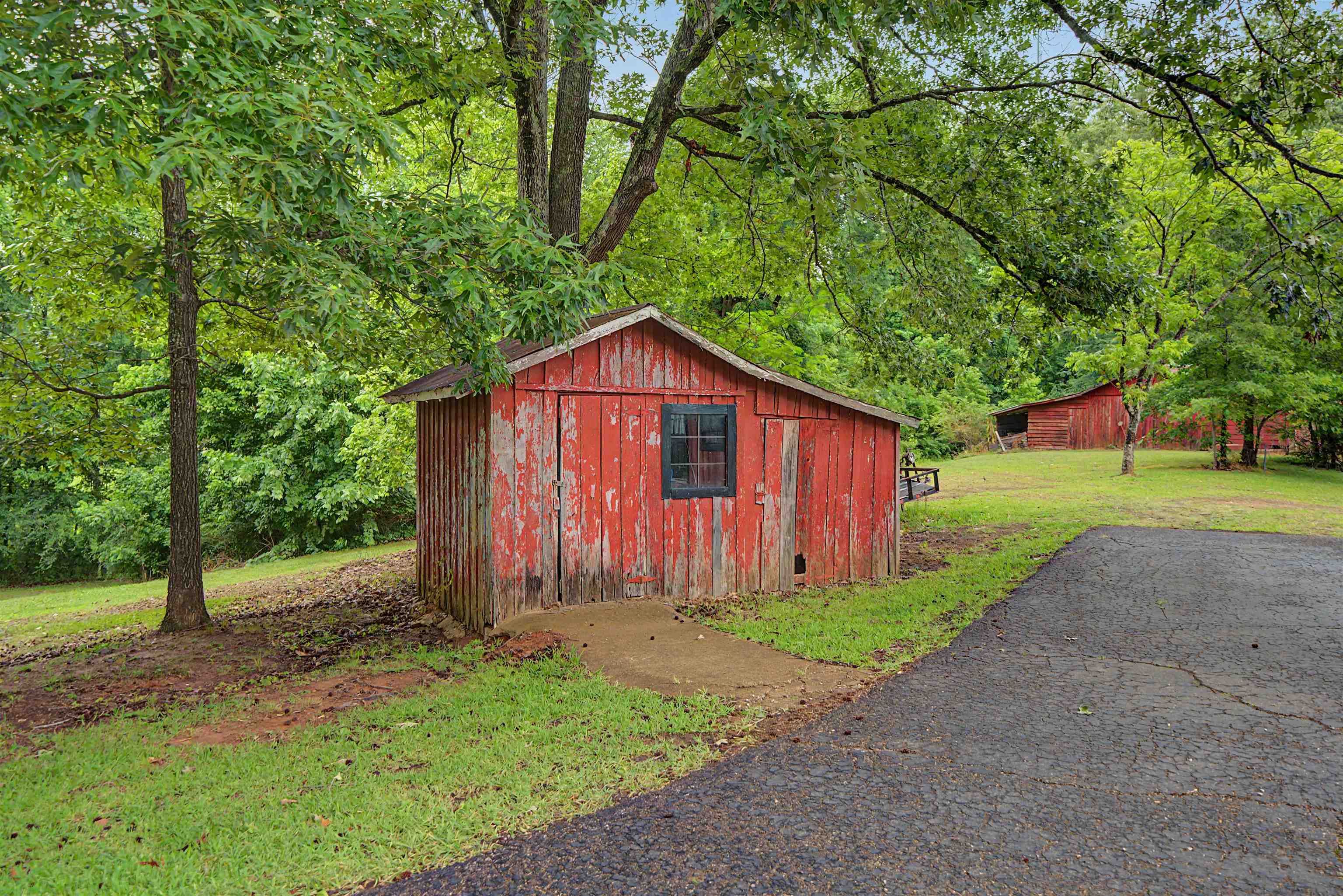 336 57th Highway West Ramer, TN 38367 - Photo 34 of 39 Red-sided outbuilding featuring a dark-framed window, surrounded by mature trees and verdant landscaping