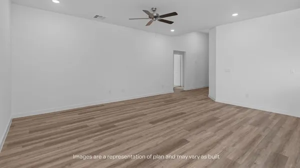 an empty room with wooden floor ceiling fan and kitchen view