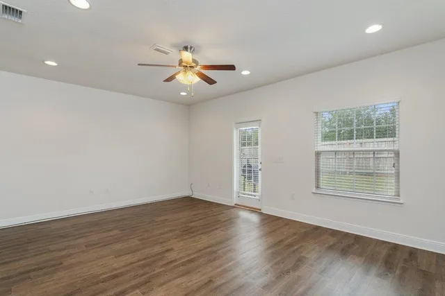an empty room with wooden floor fan and windows