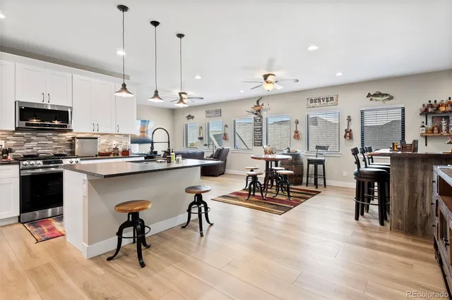 a kitchen with stainless steel appliances kitchen island granite countertop a refrigerator a stove a sink a dining table and chairs with wooden floor