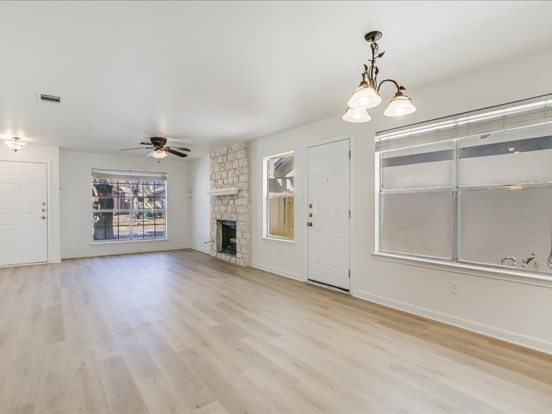 817 Smoke Signal Pass Pflugerville, TX 78660 - Photo 2 of 10 Unfurnished living room with a stone fireplace, ceiling fan, light wood-style flooring, and suspended lighting