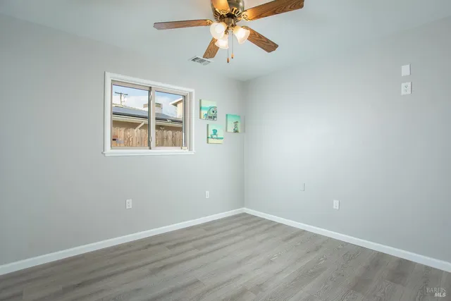 an empty room with wooden floor chandelier fan and windows