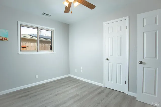 an empty room with wooden floor chandelier fan and windows