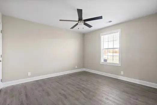 an empty room with wooden floor ceiling fan and windows