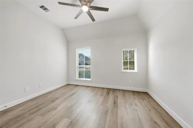 an empty room with wooden floor fan and windows