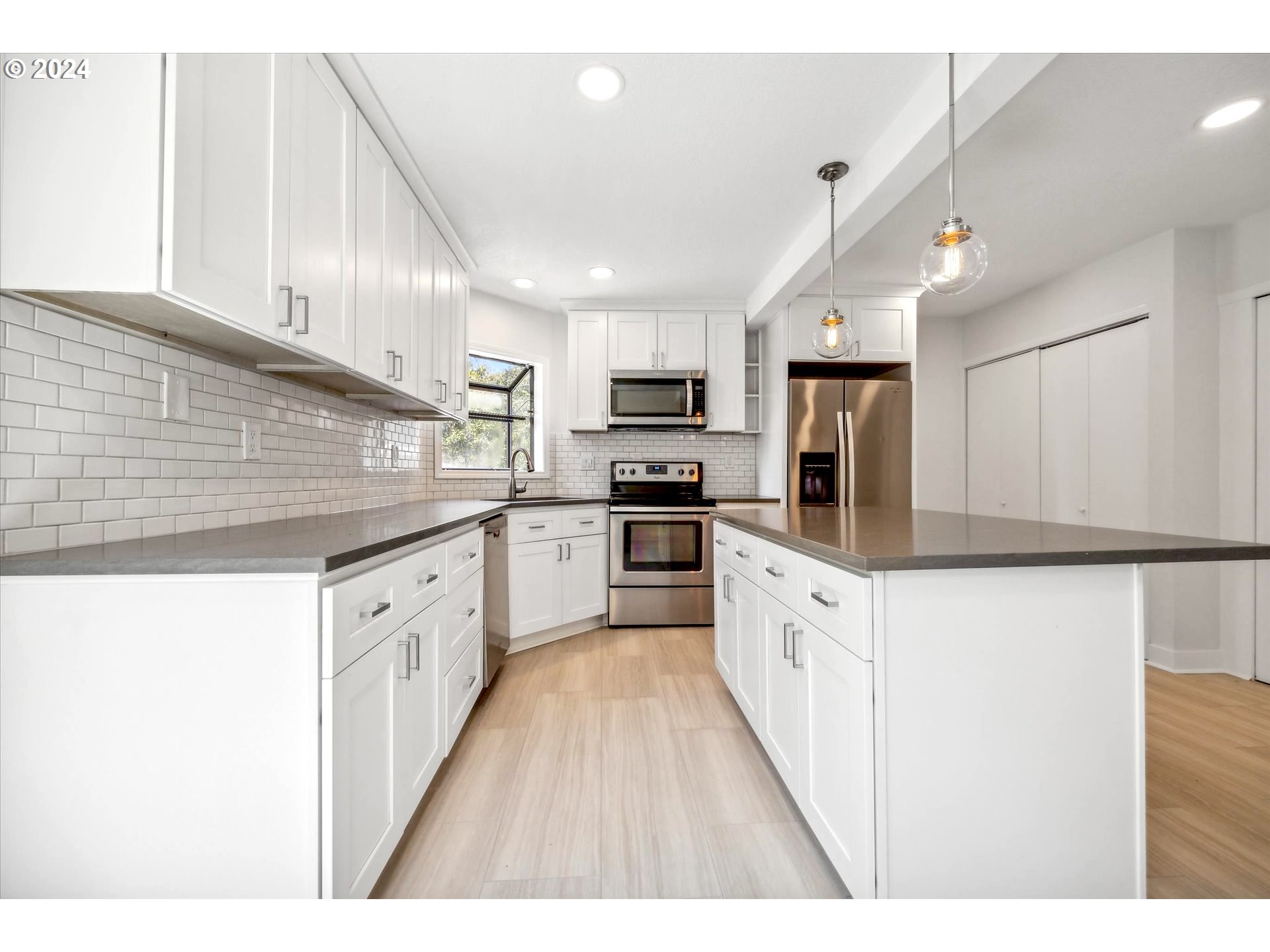 10097 Southwest Walker Road Portland, OR 97225 - Photo 6 of 44 a large kitchen with stainless steel appliances kitchen island a sink dishwasher a refrigerator and white cabinets with wooden floor