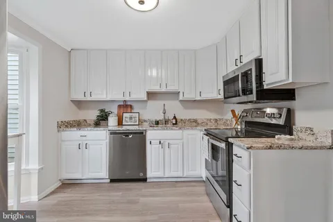 a kitchen with stainless steel appliances granite countertop a stove top oven a sink dishwasher and a refrigerator with white cabinets