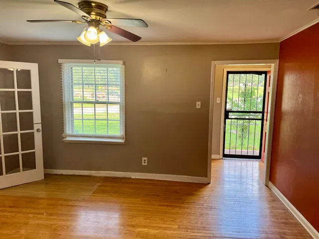 an empty room with wooden floor chandelier fan and windows
