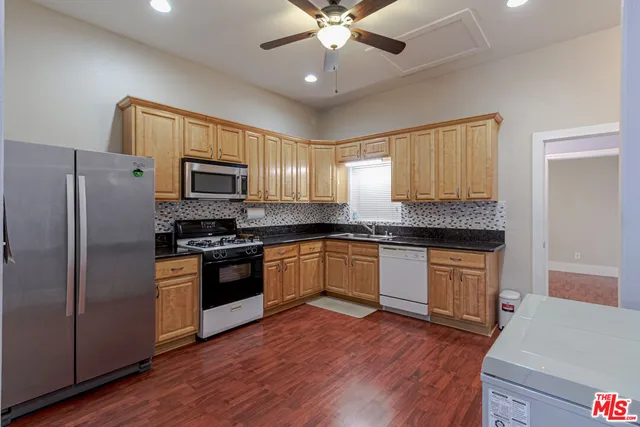a kitchen with granite countertop a refrigerator a sink dishwasher a stove and a microwave oven with wooden floor